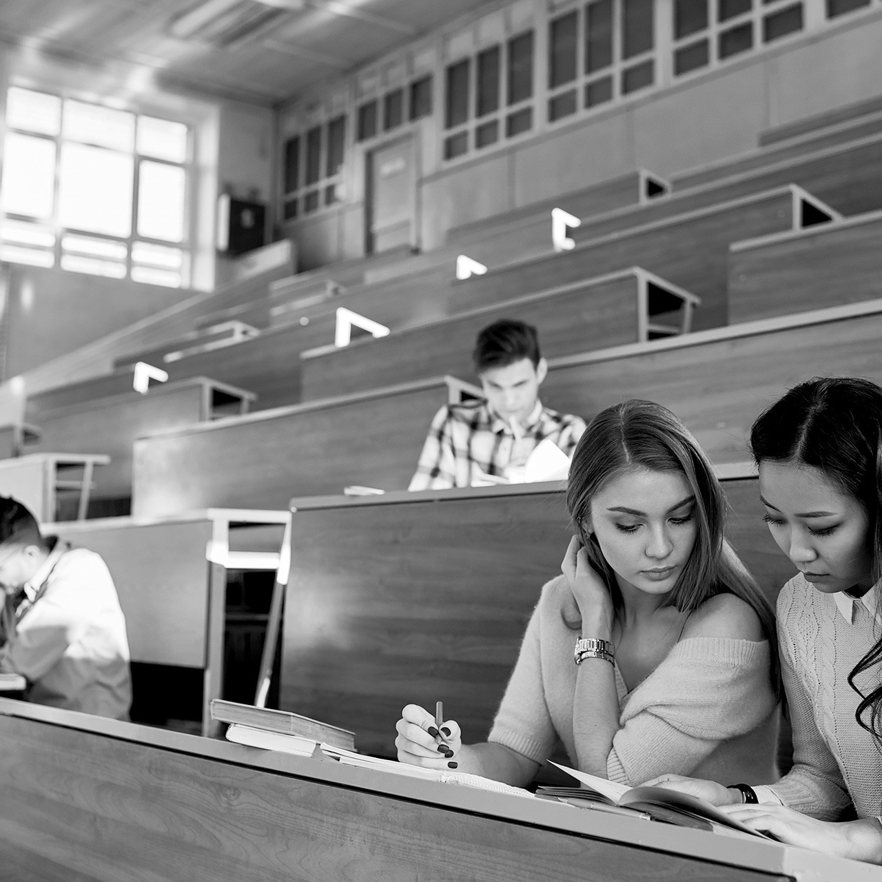 Two women sitting close together in a lecture hall sharing a book